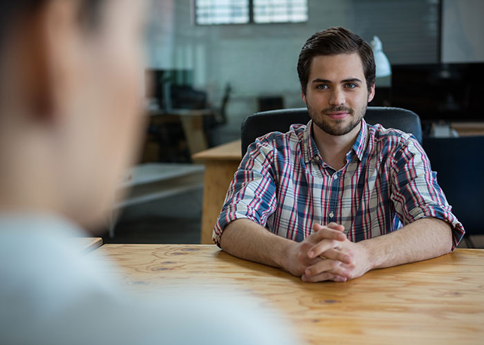 Young man in a plaid shirt sitting at a table, symbolizing a jobless partner in a relationship discussion.
