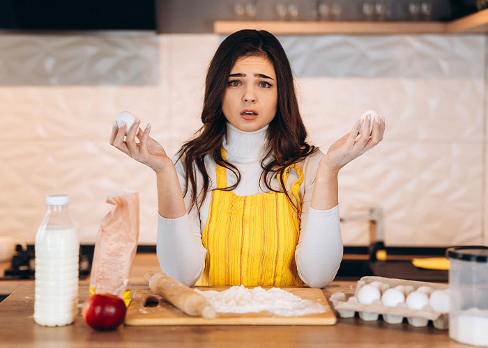 Woman in a yellow apron hesitant to cook a foreign traditional Christmas spread in a modern kitchen setting.