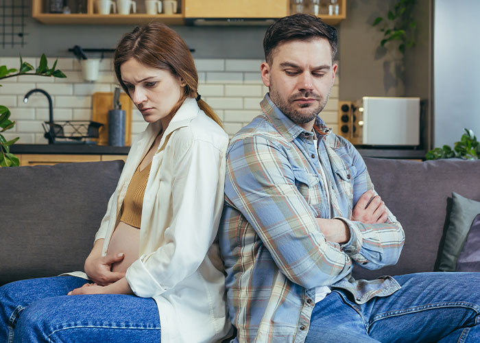 Woman looking upset and reluctant to cook a foreign traditional Christmas spread, sitting back to back with a man indoors.