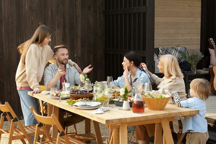 Family enjoying a lively outdoor meal prepared by wife, showcasing feast and fun with loved ones gathered around the table.