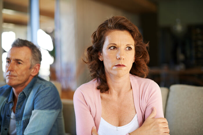 Wife looks moody while husband sits nearby after only opening oven door during family feast preparation.