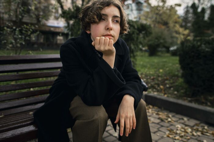 Person sitting on a bench outdoors, looking moody and contemplative, reflecting the theme of wife preparing feast and fun.