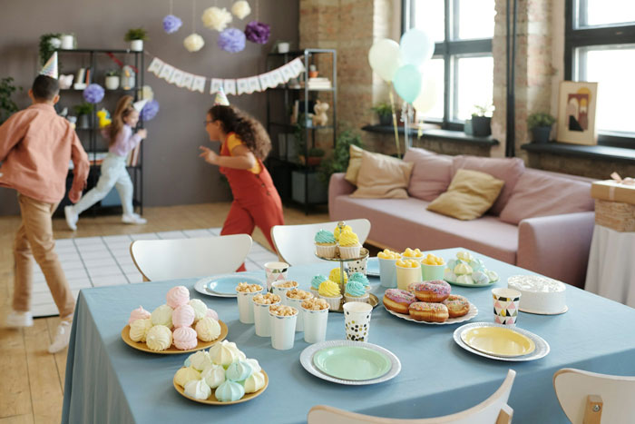Children playing at a decorated birthday party with a table full of colorful cupcakes, donuts, and snacks in a cozy room. Children playing at a decorated birthday party with a table full of colorful cupcakes, donuts, and snacks in a cozy room.