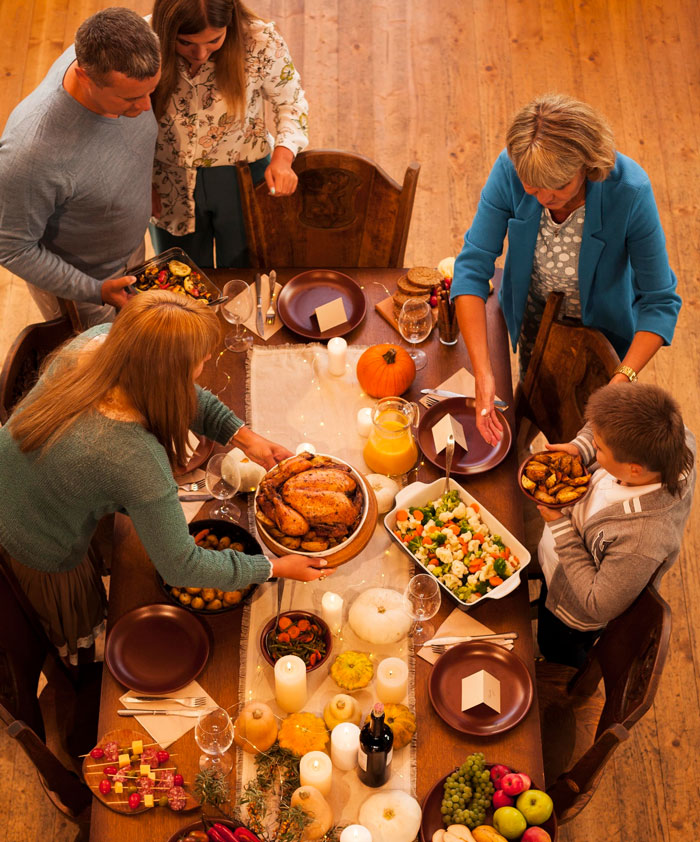 Family gathering around a traditional Thanksgiving meal with roasted turkey and autumn decorations on wooden table.