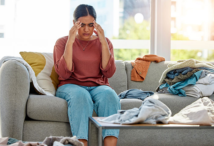 Woman stressed sitting on couch surrounded by messy clothes, facing challenges with mooching adult stepkids at home.