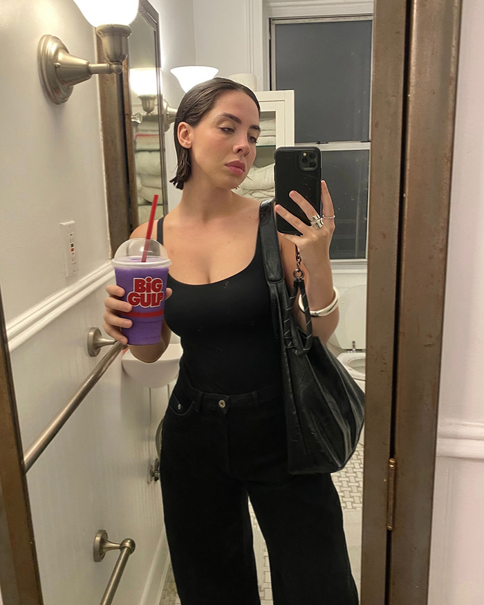 Woman taking mirror selfie holding a purple Big Gulp drink, showing a feminist tattoo rule sparking internet debate.