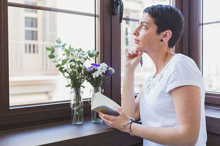 Woman holding a book, sitting by a window, thoughtfully planning a walk home with daughter or friend.