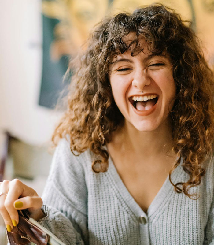 Woman with curly hair laughing joyfully, capturing the moment related to woman took back nephews Christmas gift.
