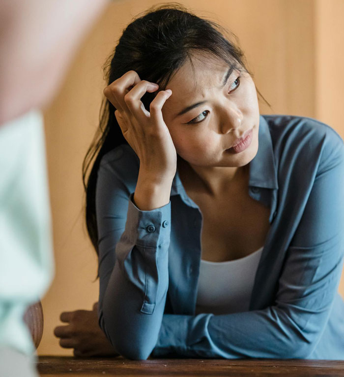 Woman took back nephew's Christmas gift, looking thoughtful and concerned while sitting at a wooden table indoors.