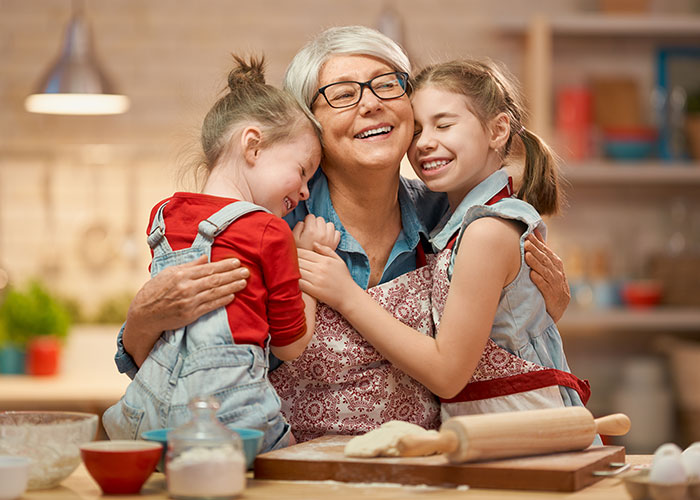 Grandma babysitting kids in kitchen, hugging two smiling children while baking with rolling pin and dough on table. Grandma babysitting kids in kitchen, hugging two smiling children while baking with rolling pin and dough on table.