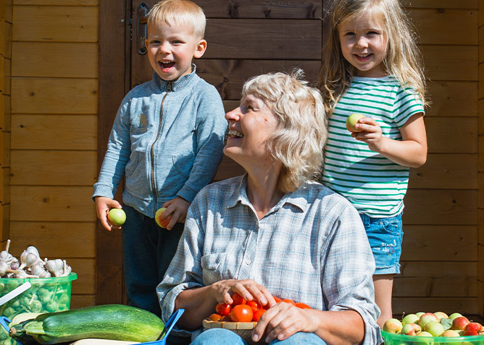 Grandma babysitting five kids outside, holding tomatoes and surrounded by fresh vegetables on a sunny day. Grandma babysitting five kids outside, holding tomatoes and surrounded by fresh vegetables on a sunny day.