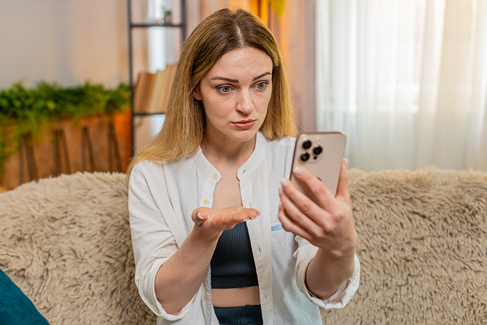 Woman looking frustrated at her smartphone while sitting on a couch, relating to a car borrowing dispute story. Woman looking frustrated at her smartphone while sitting on a couch, relating to a car borrowing dispute story.