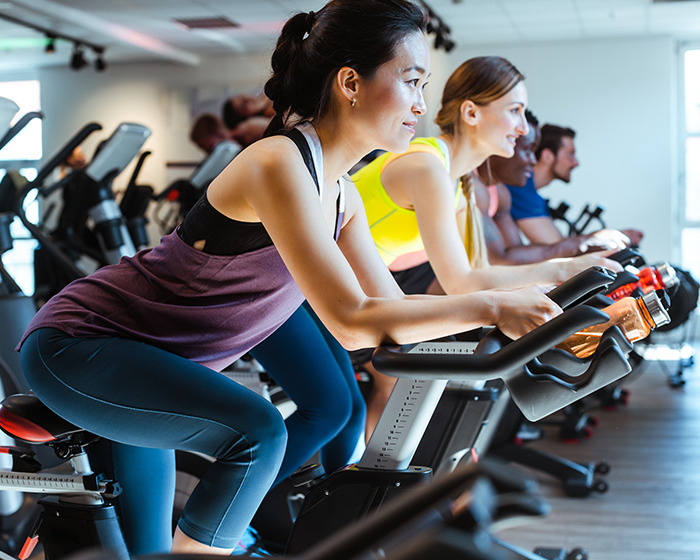 Group of people wearing activewear cycling indoors with focus on woman, illustrating trending activewear in public debate.