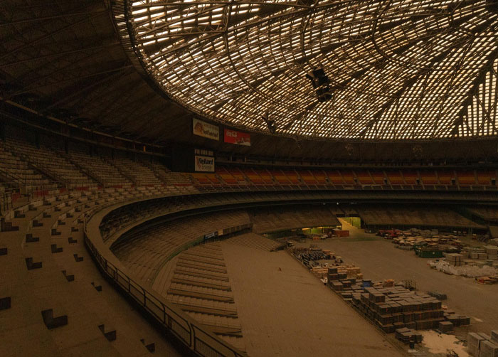 Empty abandoned stadium with scattered debris and lighting filtering through a large curved roof, showing a place causing worst night sleep.