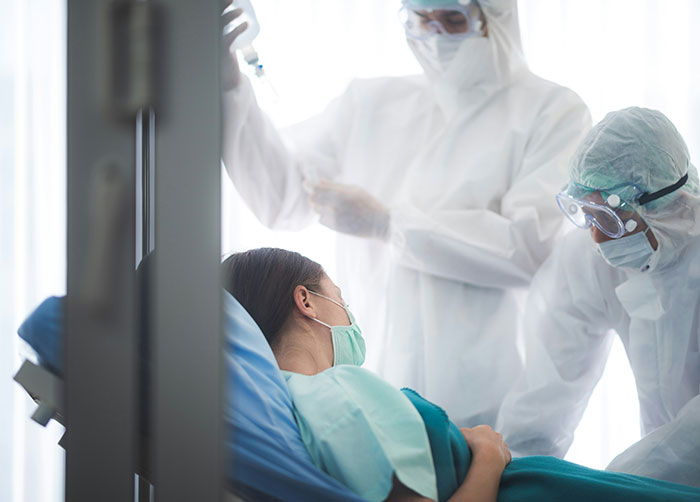 Patient wearing a mask in hospital bed with medical staff in protective gear illustrating worst night's sleep places.