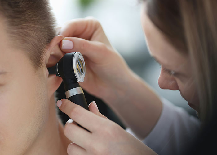 Doctor examining a patient's ear closely, highlighting potential causes of a worst night’s sleep due to place-related factors.