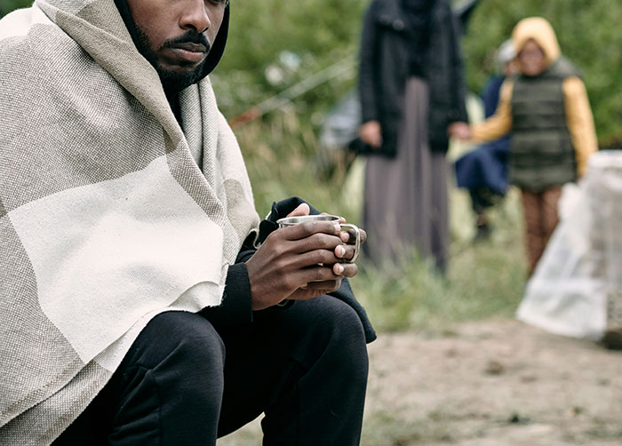 Man wrapped in a blanket holding a cup outdoors, illustrating people having the worst night’s sleep because of their place.