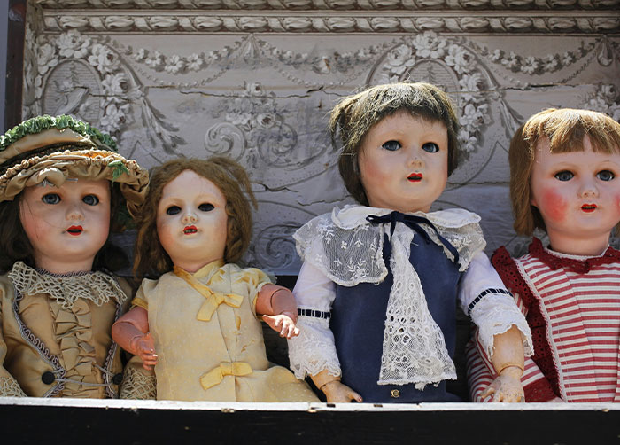 Four vintage creepy dolls in old clothing displayed on a shelf illustrating worst night’s sleep places.