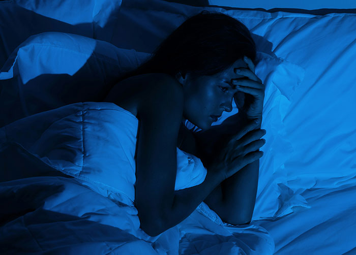 Woman lying awake in bed at night, struggling to sleep due to the uncomfortable place she was in.