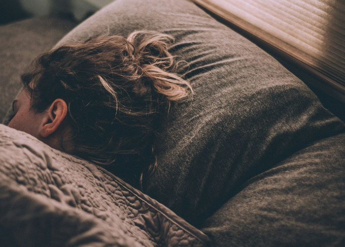 Person struggling to sleep in bed under a blanket, illustrating the worst night’s sleep due to the place they were in.