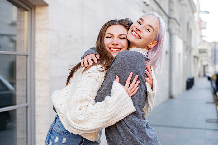 Two women smiling and hugging outdoors, highlighting cousin's family accusing woman of stealing spotlight with baby and ring.