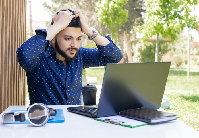 Man with worried expression using laptop outdoors, illustrating the impact of internet rabbit holes on people's lives.