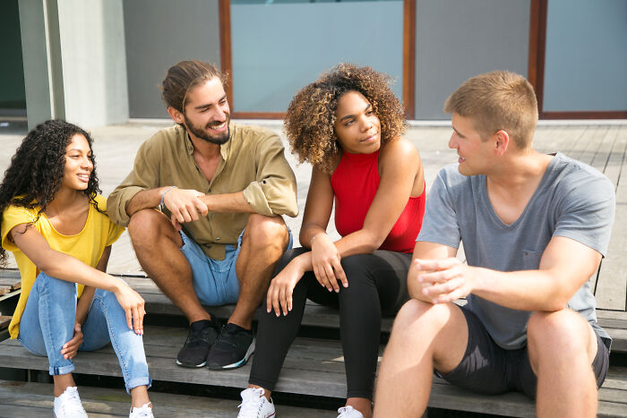 Group of young adults enjoying a casual college experience outdoors while sitting and chatting on wooden steps.