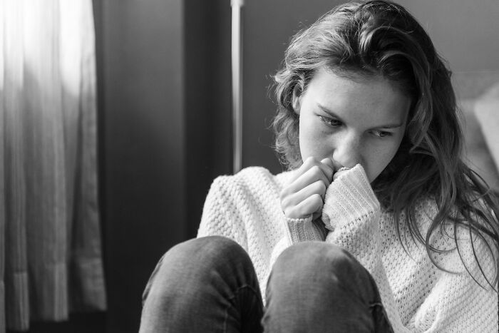 Thoughtful young woman sitting alone by the window, reflecting on emotions only adopted people understand deeply.