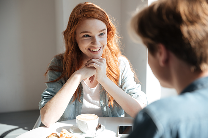 Young woman smiling at a man during a coffee meeting, illustrating a loyalty test in a longtime friendship scenario.