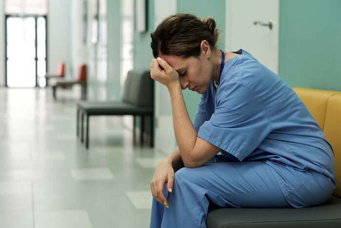 Stressed medical professional sitting alone in hospital hallway reflecting on eerie patient statements that haunt doctors.