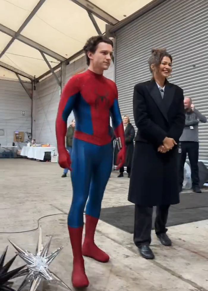 Tom Holland dressed as Spider-Man standing next to Zendaya in a black coat, sparking pregnancy rumors in leaked video.