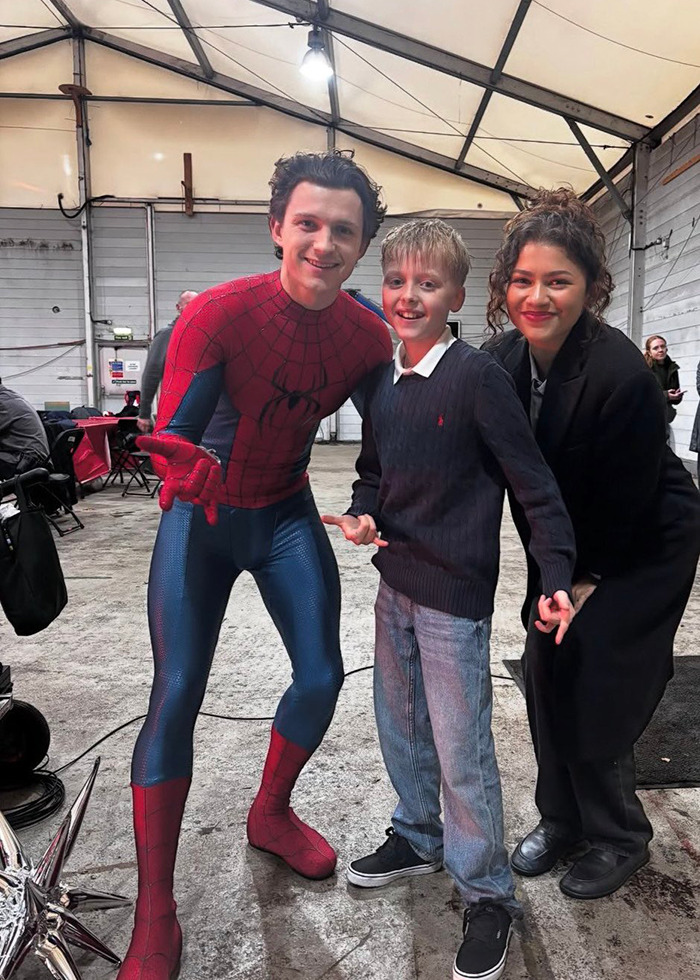 Tom Holland in Spider-Man suit with Zendaya and a young fan on film set, sparking pregnancy rumors online.
