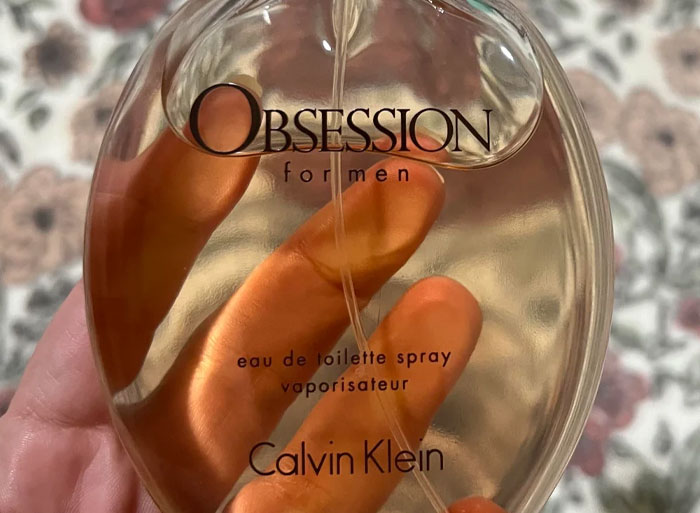 Hand holding a Calvin Klein Obsession for men bottle with a blurred floral background, related to zoo employee insights.