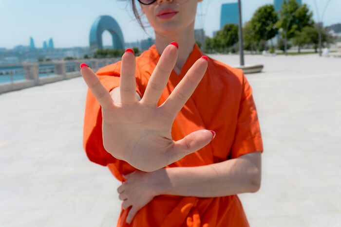 Woman in orange shirt showing hand in outdoor urban setting, representing positive stereotypes about various countries.