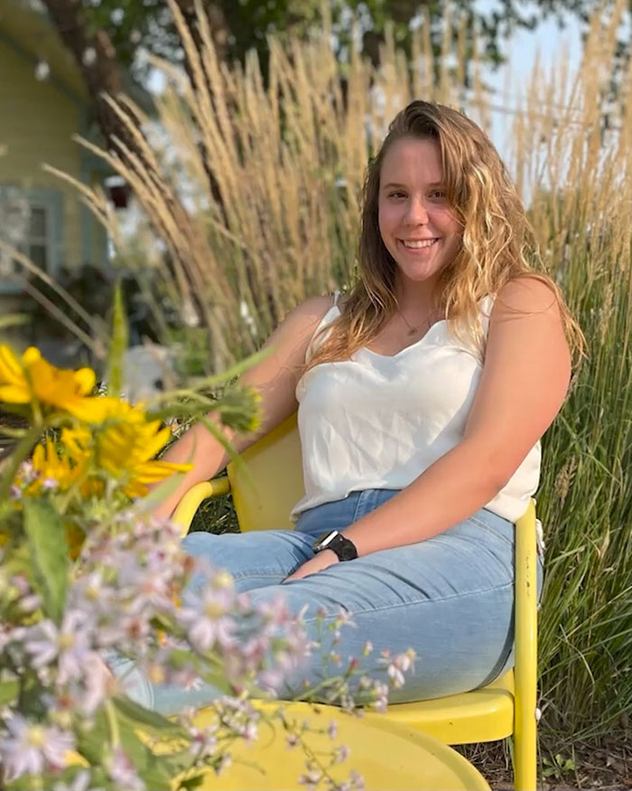 Young woman sitting outdoors in a yellow chair surrounded by flowers, related to engaged teacher who sent 35K texts to student.