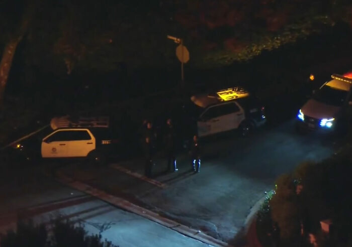Police officers stand near patrol cars at night, highlighting MAGA hypocrisy in Rob Reiner and Charlie Kirk comparisons.