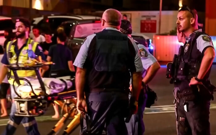 Police officers and paramedics respond at night to an incident related to Bondi Beach attack causing public outrage.