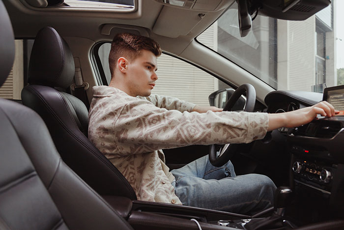 Young man sitting in a car looking focused while adjusting the dashboard, highlighting half-brother car theft conflict.