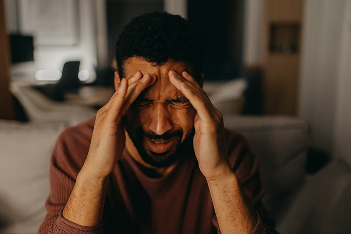 Man in brown sweater sitting indoors, holding his head in distress, illustrating family intervention and uncomfortable truth.