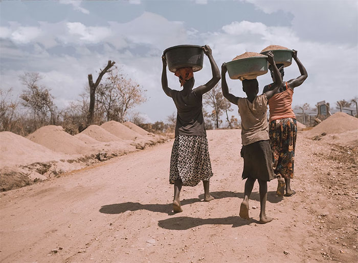 Three women in an African country carrying baskets on their heads, representing a simple lifestyle and daily labor.