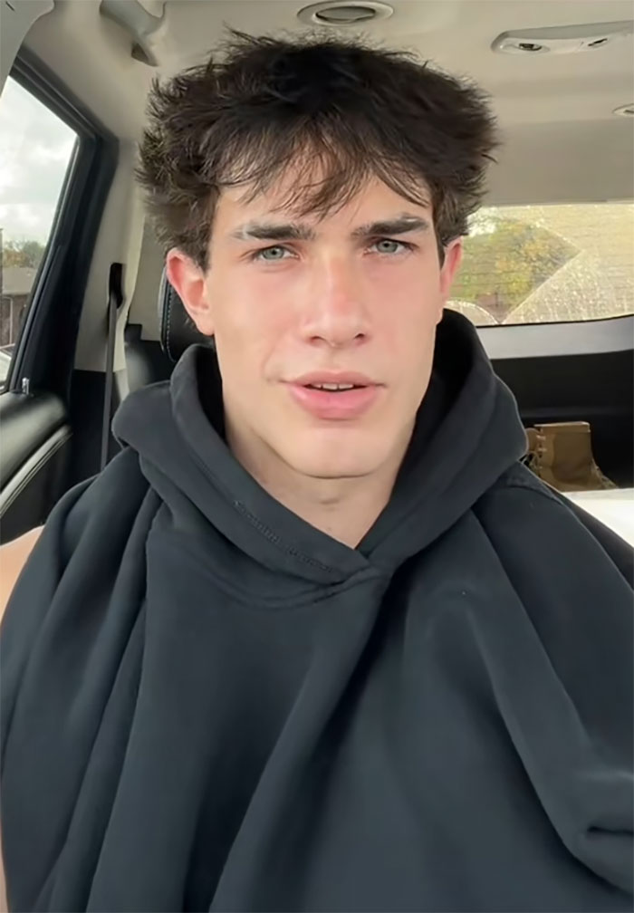 Young man with messy hair wearing a black hoodie inside a car, sharing a story about a waiter serving first date disaster. Young man with messy hair wearing a black hoodie inside a car, sharing a story about a waiter serving first date disaster.