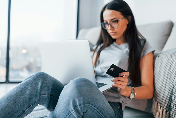 Young woman holding credit card and using laptop at home, illustrating concept of marriage treated like ATM machine.