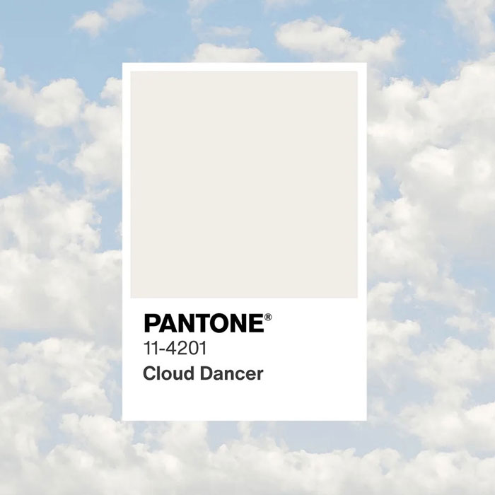 Pantone Cloud Dancer color swatch displayed against a cloudy sky background highlighting the controversial Color of the Year.