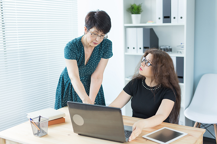 Middle-aged woman discussing wedding illustration plan with younger woman at computer, artist catching on to MIL&rsquo;s plan.