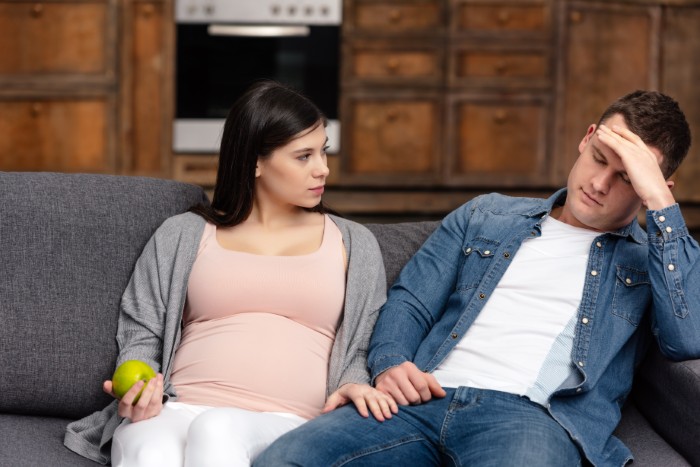 Pregnant woman looks frustrated while husband won&rsquo;t stand up to his mother, causing tension in their relationship at home.
