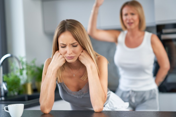 Woman upset at kitchen counter with another woman angrily gesturing, illustrating husband not standing up to his mother conflict.