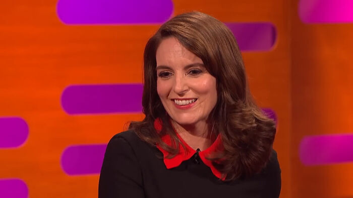 Woman with brown hair and red collar smiling during a TV interview about fascinating secrets about celebrities.