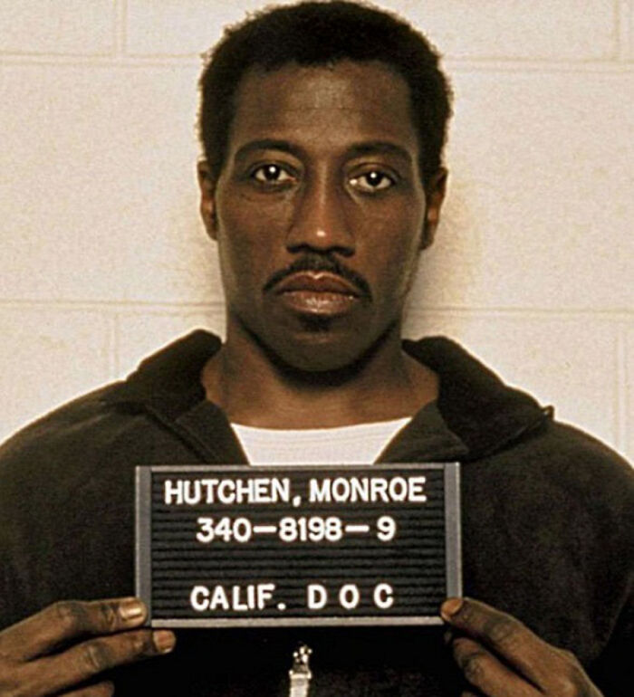 Mugshot of a celebrity named Monroe Hutchen holding a board with arrest details against a plain background.