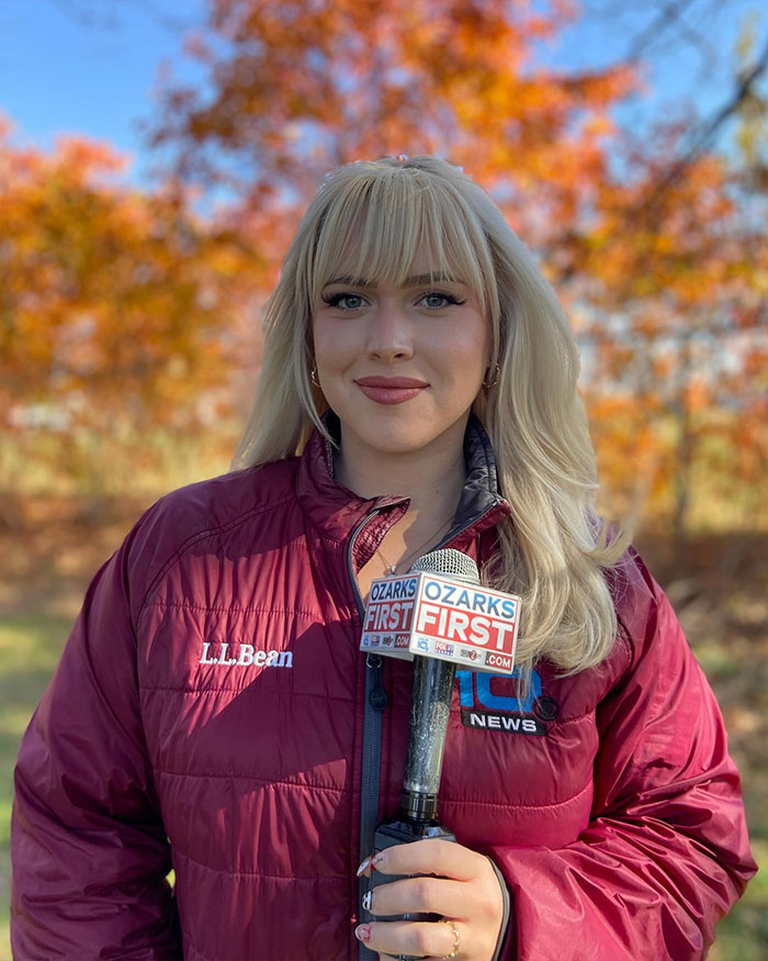 Curvy news anchor outdoors holding Ozarks First microphone with fall trees in the background during a broadcast. Curvy news anchor outdoors holding Ozarks First microphone with fall trees in the background during a broadcast.