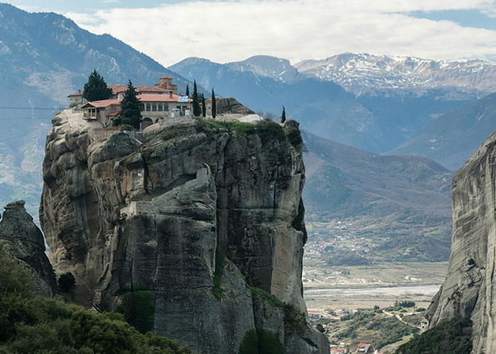 Monastery perched on a tall rock formation with mountains in the background, a place that looks AI generated but is real.